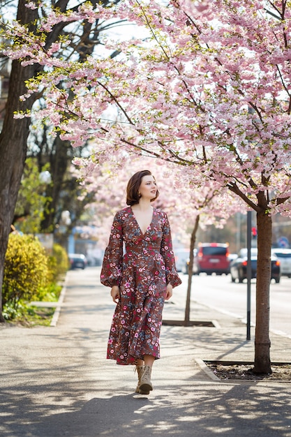 Bella giovane donna in un vestito in alberi di sakura in fiore. fuori è una calda giornata di sole primaverile