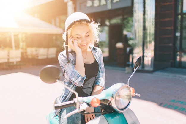 Beautiful young woman dressed casual sitting on scooter and talking on phone