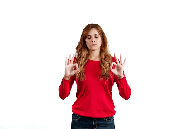 Beautiful young woman dressed in a red sweater, concentrated and meditating, isolated on a white background