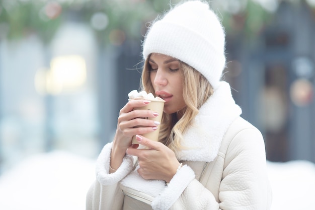 屋外でホットココアを飲む美しい若い女性。クリスマス。