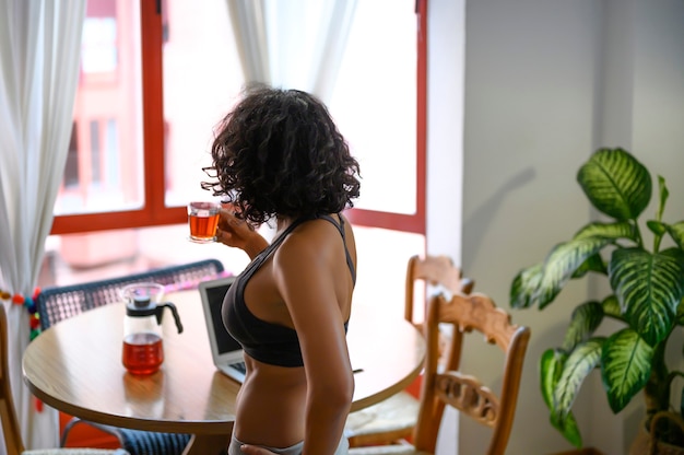 Beautiful young woman drinking tea near window at home