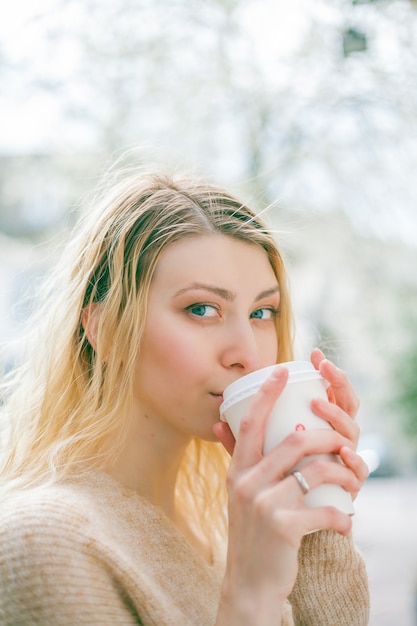 美しい若い女性はヨーロッパの都市の通りに行くためにコーヒーを飲みます