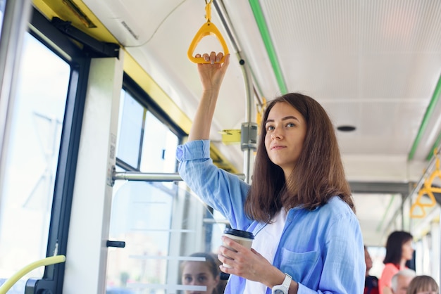 Beautiful young woman drinks delicious coffee in city bus or tram. Concept of public transport.