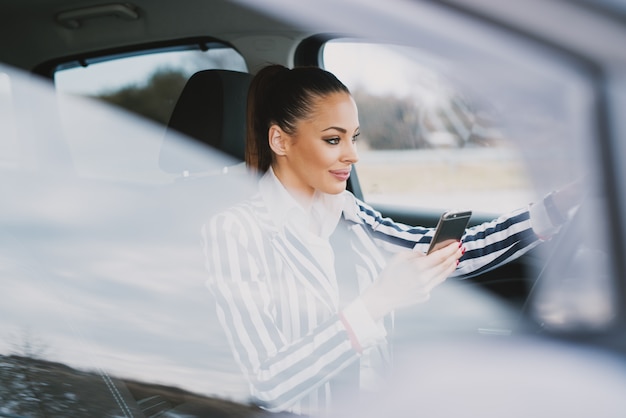 運転の美しい若い女性と街でテキストメッセージ。