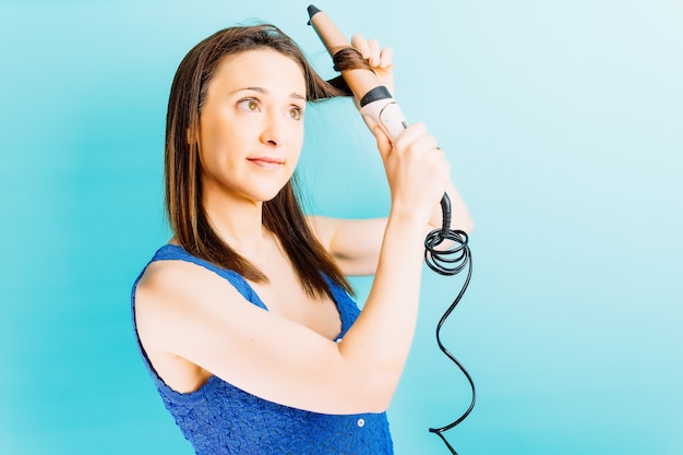 Beautiful young woman drying her hair with a hair curler blue background