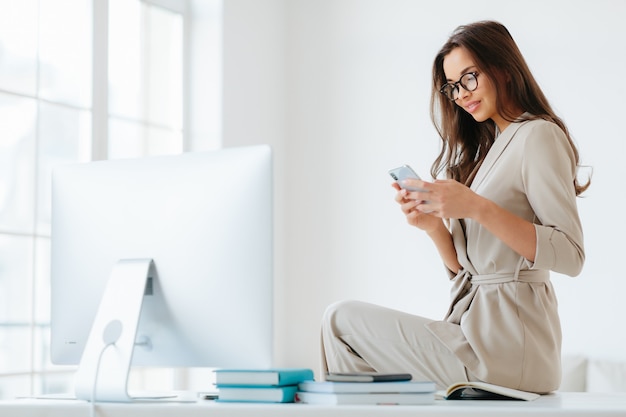 Beautiful young woman in elegant clothes checks newsfeed via smartphone