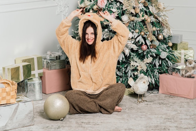 Beautiful young woman in an elegant dress standing next to christmas tree and presents.