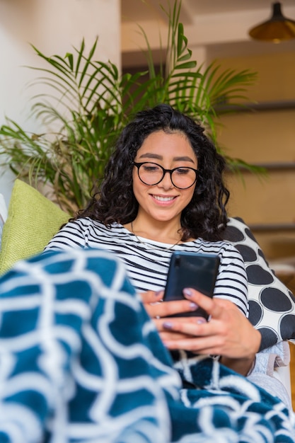 自宅のソファに横になってスマートフォンで入力を楽しんでいる美しい若い女性