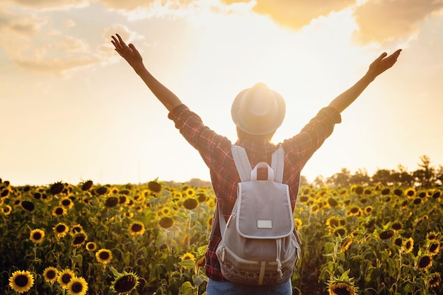 Beautiful young woman enjoying nature on the field of sunflowers at sunset