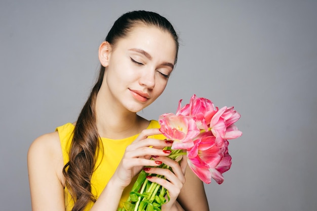 目を閉じてピンクの花を持って春を楽しんでいる美しい若い女性