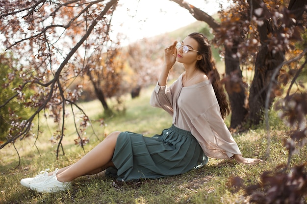 Bella giovane donna che gode di una soleggiata giornata di primavera in un parco durante la stagione della fioritura dei ciliegi