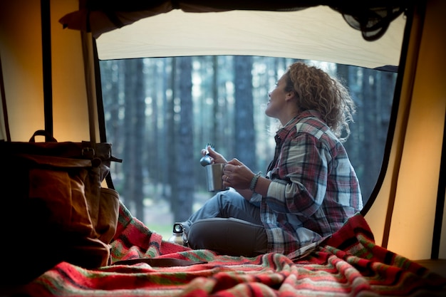 Beautiful young woman enjoys the forest nature at the entrance of her tent in the woods