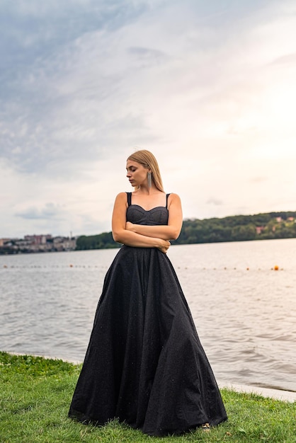 Bella giovane donna in abito nero lungo da sera vicino allo stile di vita estivo dello stagno