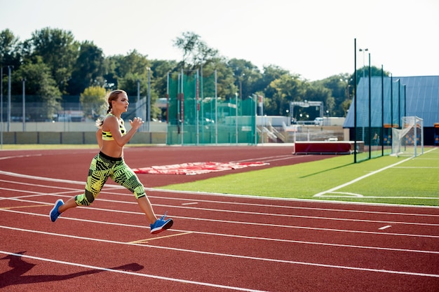 美しい若い女性は、スタジアムのアスレチックトラックでジョギングやランニングをします。