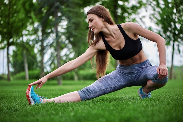 Bella giovane donna che si esercita all'aperto allungando una delle sue gambe