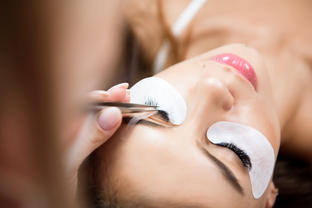 Beautiful young woman during eyelash extension in a salon.