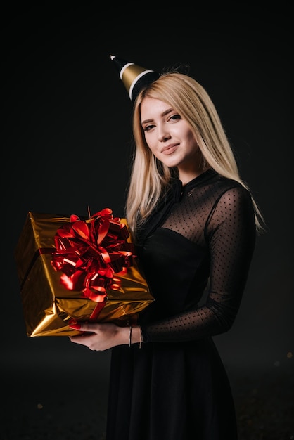 Beautiful young woman in a festive cap holds a holiday box with a gift