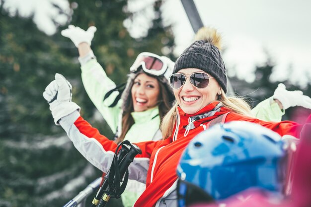 겨울 방학을 즐기는 아름다운 젊은 여자 친구. 그들은 스키 리프트에 운전 하 고 미소로 카메라를 찾고 있습니다.