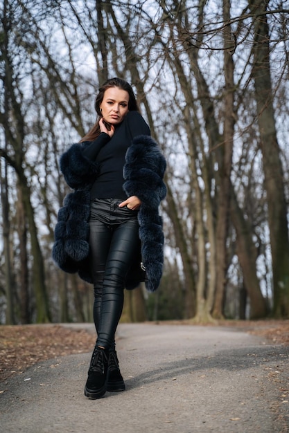 beautiful young woman in fur coat and leather pants walks in the park