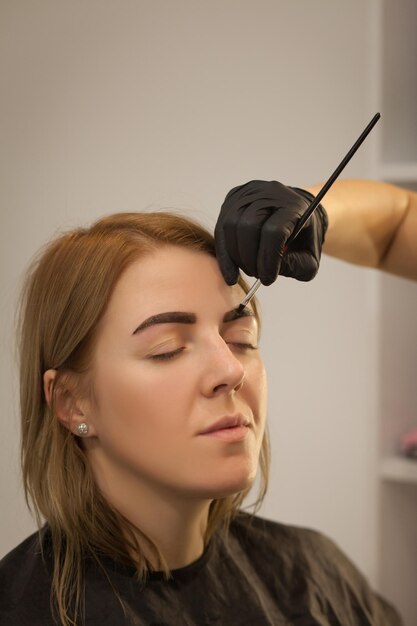 Beautiful young woman gets eyebrow correction procedureYoung woman painting her eyebrows in beauty salon