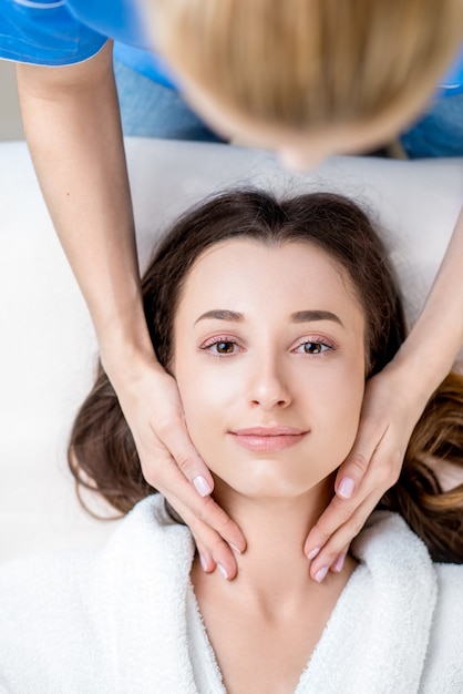 Beautiful young woman getting facial massage lying on the couch. Top view focused on the face