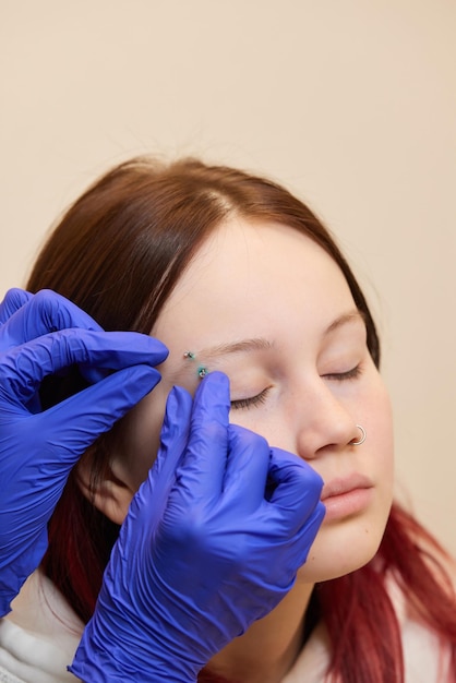 Beautiful young woman getting her eyebrow pierced body piercer wearing blue gloves