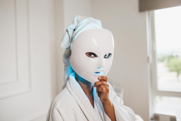 Beautiful young woman getting a led light therapy mask treatment  for her face at the beauty salon.