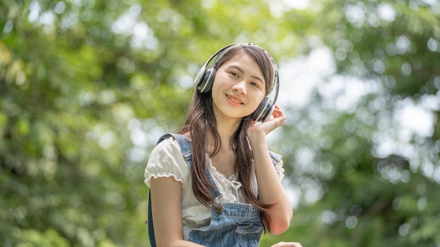 緑の都市公園の背景でポーズをとるベージュのシャツの美しい若い女性の女の子笑顔の女の子聞く