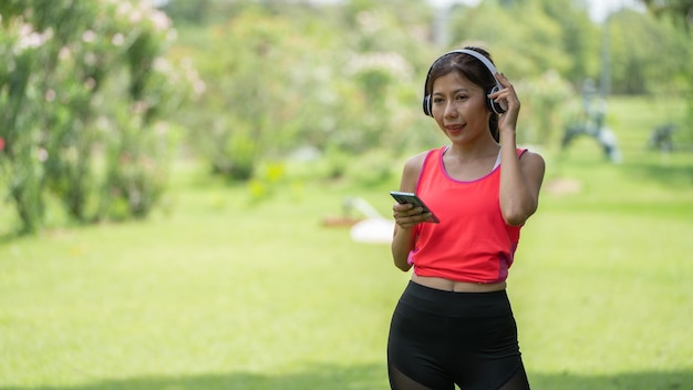 Beautiful young woman girl in beige shirt posing in Green city Park background Smile girl Listening Music with Headphones feeling Touching Happiness People lifestyle concept Mock up copy space