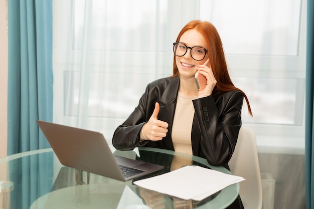 beautiful young woman in glasses with red hair at the table with a laptop in the office