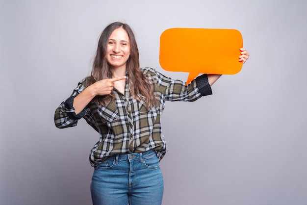 Beautiful young woman in green shirt pointing at empty speech bubble.