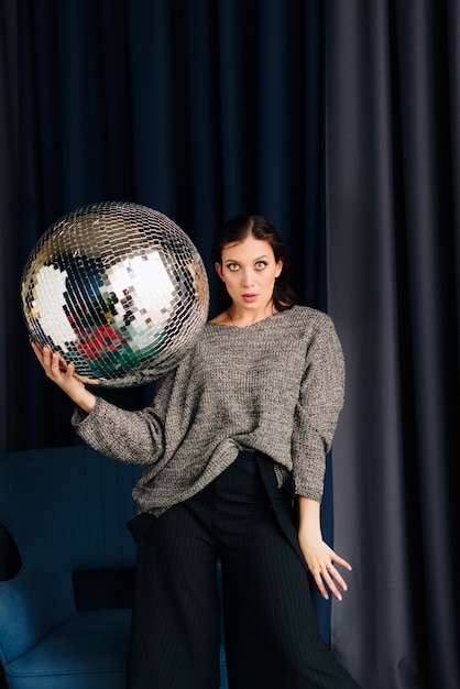 Foto bella giovane donna in maglione grigio e palla da discoteca a casa