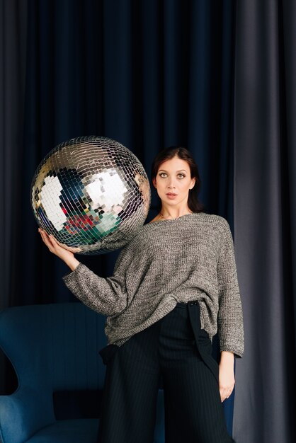 Foto bella giovane donna in maglione grigio e palla da discoteca a casa