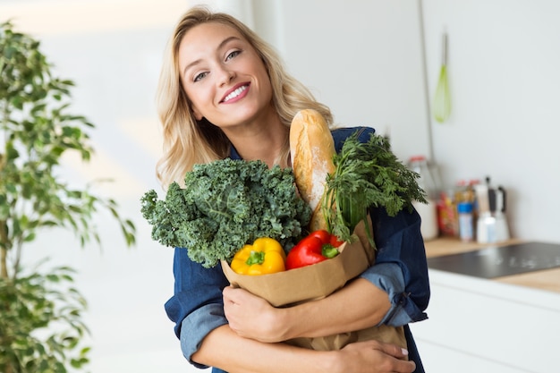 家庭で野菜と美しい若い女性の食料品の買い物袋。