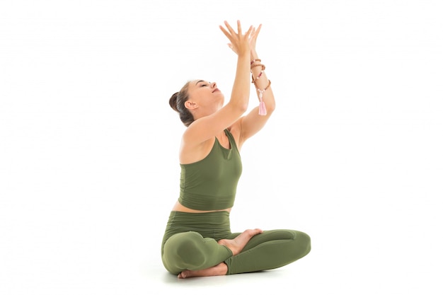 Photo a beautiful young woman gymnast with dark long hair stuffed into a bundle in a green sports elastic suit sits and gets energy from meditation