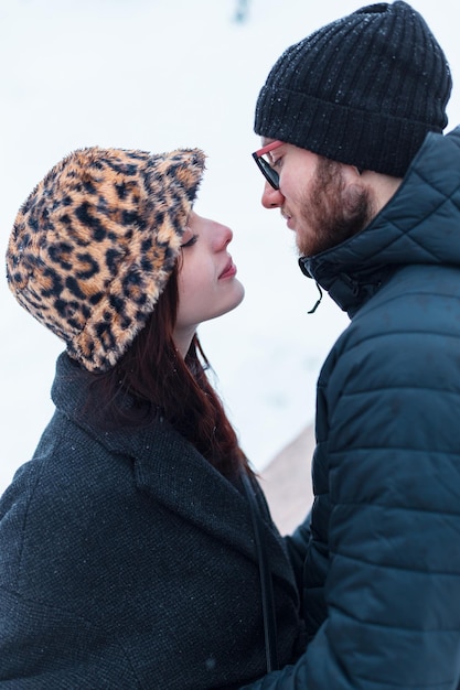 Красивая молодая женщина и симпатичный мужчина в модной зимней одежде с курткой и шляпой обнимаются на белом фоне со снегом в парке пара влюбленных на открытом воздухе