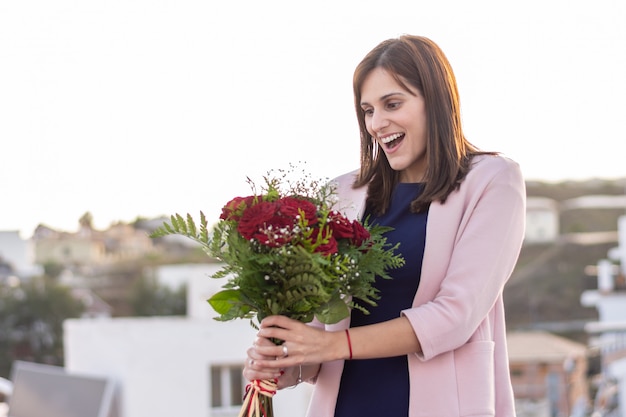 美しい若い女性は幸せで、赤いバラの彼女の花束に驚いた