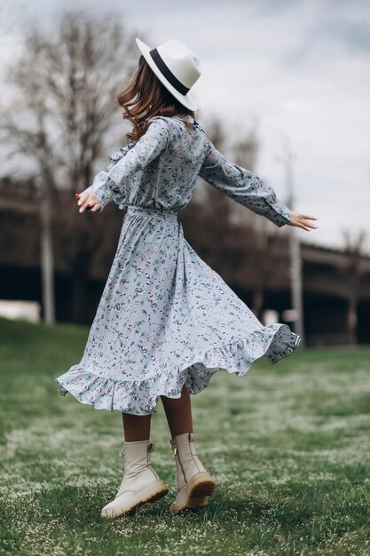 Beautiful young woman in a hat and a blue dress is dancing in a field of wildflowers Spring