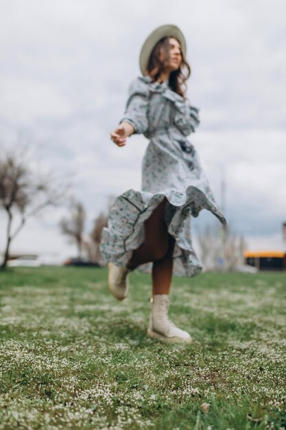 A beautiful young woman in a hat and a blue dress runs through a field of wildflowers blure