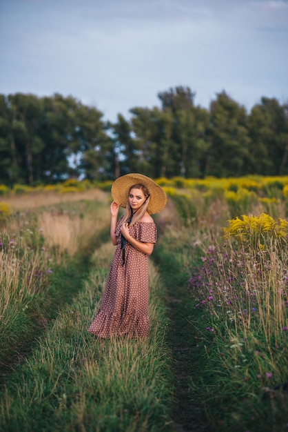 Beautiful young woman in a hat and dress walks in nature in autumn.