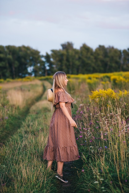 Beautiful young woman in a hat and dress walks in nature in autumn.