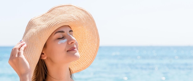 Beautiful young woman in hat is applying sunblock under her eyes and on her nose like Indian Sun protection concept