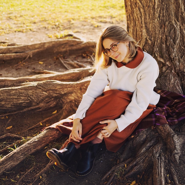 Beautiful young woman have a leisure posing in autumn park dressed in long brown skirt and white sweater