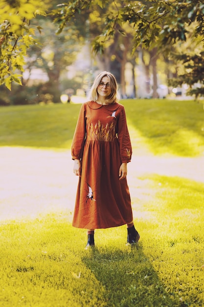Красивая молодая женщина гуляет по осеннему парку, одетая в длинное коричневое платье
