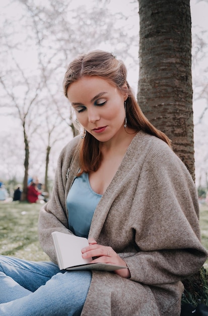 Beautiful young woman having picnic and reading book on sunny spring day in park during cherry blossom season Cherry blossom festival Outdoor recreation