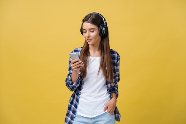 Beautiful young woman in headphones listening to music and singing on yellow background