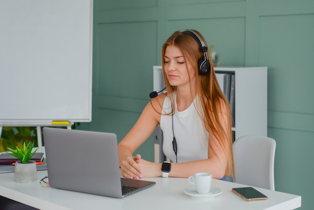 beautiful young woman in a headset communicates online with a laptop in the office lifestyle f