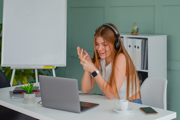 beautiful young woman in a headset communicates online with a laptop in the office lifestyle f