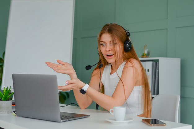 beautiful young woman in a headset communicates online with a laptop in the office lifestyle f