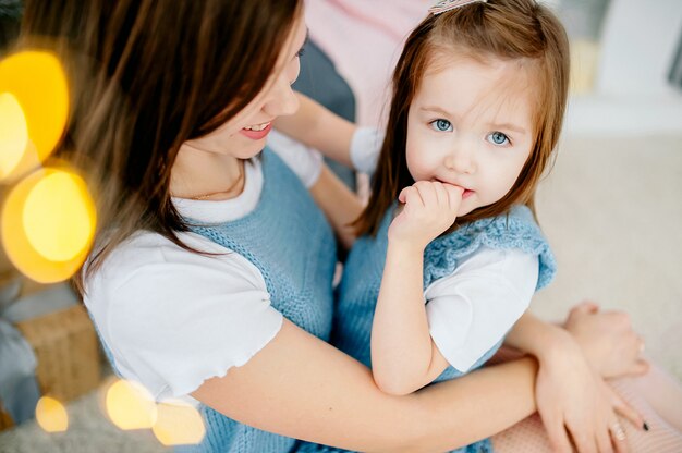 La bella giovane donna e la sua piccola figlia affascinante stanno abbracciando nello stesso sorridere degli abiti. vacanze di natale